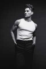 Wall Mural - Monochrome portrait of a handsome young man with stylish haircut in a white undershirt and black pants. Studio shot.