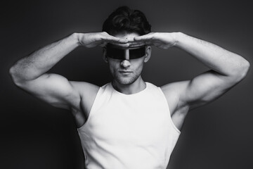 Wall Mural - Monochrome portrait of a handsome young man with stylish haircut in a white undershirt, black pants and glasses. Studio shot.