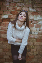 Confident Brunette Woman Leaning Forward On Brick Wall Background Wearing A Fuzzy Turtleneck Sweater