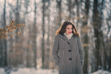 Poster - Shallow focus shot of a beautiful Caucasian woman wearing a coat posing in the snowy forest