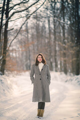 Wall Mural - Full body shot of a brunette girl in a stylish winter outfit walking down the forest path in winter