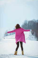 Canvas Print - Crazy young brunette girl dancing arms wide open in the snowy forest wearing a pink coat