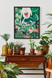 © FollowTheFlow - Domestic interior of living room with vintage retro shelf, a lot of house plants, cacti, wooden mock up poster frame on the white wall and elegant accessories at stylish home garden. Template.
