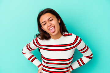 Young Indian woman isolated on blue background funny and friendly sticking out tongue.