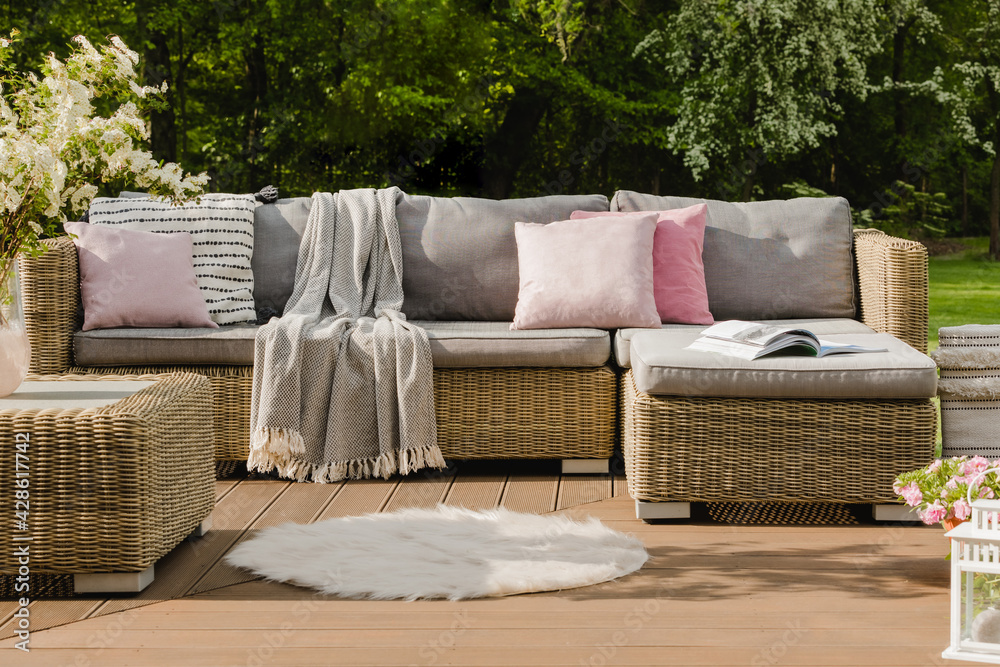 Pastel pink pillows on grey sofa in green garden with wooden terrace - obrazy, fototapety, plakaty 