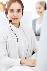 Wall Mural - Call center in sunny office. Group of diverse operators at work. Beautiful woman in headset communicating with customers of telemarketing service