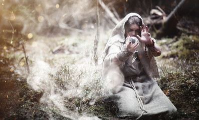 Fairy magician. A sorcerer with a glass sphere, a magical spell and a ritual. Elder with a staff and a cross in the forest. Black and white magic. A spell in an old book.