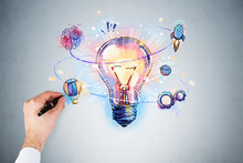 Businessman Hand Drawing Colorful Light Bulb As A Concept Of New Idea For Start Up. Concept Of Creativity And Brainstorming. Light Blue Wall On Background