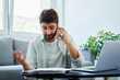 © baranq - Unhappy man discussing bills over phone. Home finances concept.