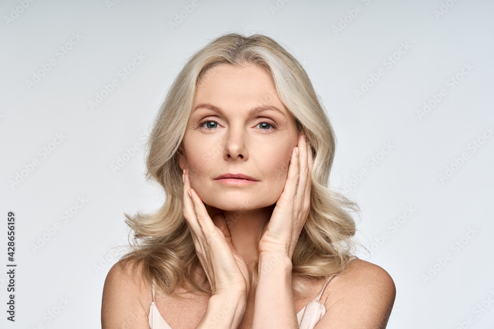 Adult senior older woman touching her perfect skin. Beautiful portrait mid 50s aged woman advertising facial anti age lift products salon care tighten skin isolated on white looking at camera. - obrazy, fototapety, plakaty 