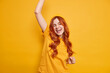 Carefree positive young ginger girl dances happily keeps arm raised closes eyes feels upbeat dressed in casual t shirt and hat poses against vivid yellow background has fun enjoys successful day