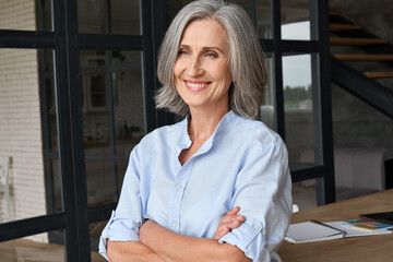 Wall Mural - smiling adult middle aged business woman standing at table posing in home office, arms crossed. port