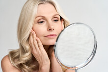 Closeup Portrait Of Gorgeous Happy Middle Age Woman Looking At Mirror Touching Her Skin Enjoying Treatment For Dry Skin. Advertising Of Antiaging Beauty Skin Care Products.