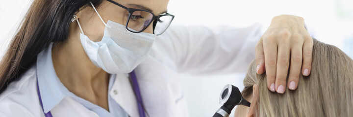 Otorhinolaryngologist looking at female patients ear with otoscope in clinic