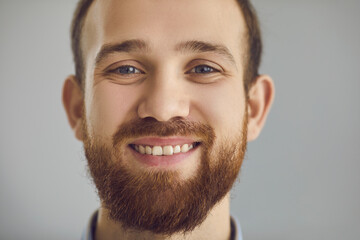 Wall Mural - Closeup studio portrait of cheerful bearded young man with friendly face smiling at camera. Head shot of happy guy with healthy natural color teeth. People's appearance and positive emotions concept