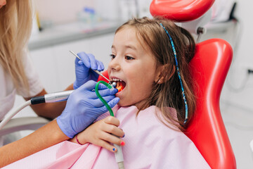 Wall Mural - Cute little girl sitting on dental chair and having dental treatment.