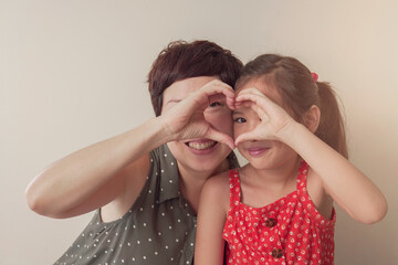 Wall Mural - Asian mother and daugther girl making heart shape gesture with hands over eyes , Happy volunteer ,donation and charity, family love, heart health insurance , mental health concept