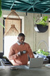 © Seventyfour - Vertical portrait of African-American man using laptop and enjoying coffee while working in eco friendly cafe interior decorated with fresh green plants