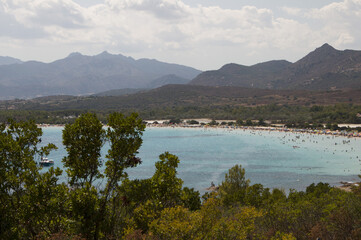 Poster - Aerial view of a seascape with swimming people surrounded by trees and mountains under a cloudy sky