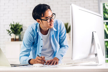 Handsome asian businessman looking at technology of laptop computer monitor while sitting on sofa.Young man creative coworker business work and typing on keyboard at home