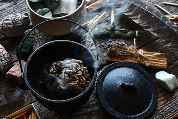 A close up image of a burning white sage smudge stick, healing crystals, and sacred feather. 