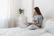 © NesolenayaAleksandra - Young beautiful pregnant woman sitting on the bed and reading a book.