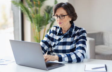 Serious elderly woman working laptop. Business woman busy working on laptop at home office