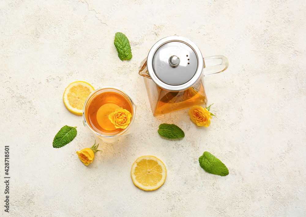 Teapot with hot tea, glass, lemon and rose flowers on light background