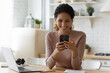 © fizkes - Overjoyed millennial hispanic female remote student learn from home take break in study to read good news at chat on cell screen. Happy young latin lady relax from distant work hold phone text message