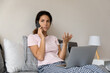 © fizkes - Work catches on weekend. Serious millennial latin woman in home clothes sit on bed with laptop on knees discuss business with colleague on phone. Young lady freelancer consult client by cell from home