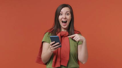 Wall Mural - Happy joyful young woman in basic casual olive green t-shirt hold using mobile cell phone say wow yes just found out great big win news doing winner gesture isolated on bright orange color background