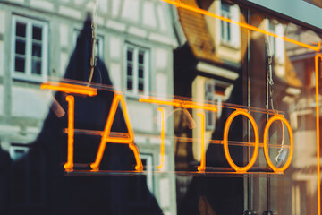 A tatoo salon with an oragen light script. Sunlight reflects on the window.

