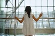 © Sirichai - The back view of cute young Asian girl in white dress, standing alone at an airport terminal looking at departing airplanes through the glass window.