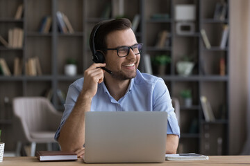 Wall Mural - smiling young caucasian male employee in headphones work distant on laptop at home office thinking d