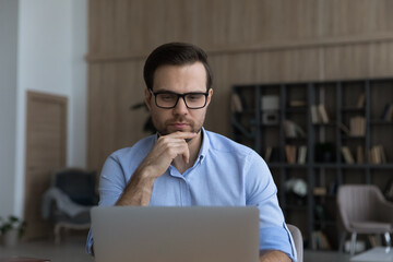 Poster - Young Caucasian man in glasses work online on computer in home office consult client customer distant. Pensive millennial male use laptop browse wireless Internet on gadget. Modern technology concept.