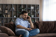 © fizkes - Young Caucasian man sit on couch at home talk speak on cellphone gadget online. Millennial male relax on sofa in living room have virtual digital conversation on smartphone. Communication concept.