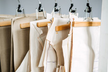 Many Paper Sewing Patterns For Different Clothes Hanging On The Rack In Sewing Factory Background. Clothing Pattern, Manufacture On Sewing Factory. Tailoring, Small Business
