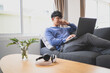 © mojo_cp - Happy young asian man using laptop sitting on sofa at his home..