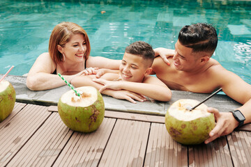 Wall Mural - Happy family of three refreshing in water on sunny summer day and drinking coconut cocktails