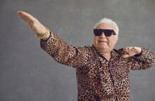 Retired Senior Man Vibing To Hype Pop Music. Portrait Of Funny Rich White Haired Old Grandpa In Cool Glasses And Leopard Patterned Party Shirt Flexing, Dancing And Having Fun On Gray Studio Background