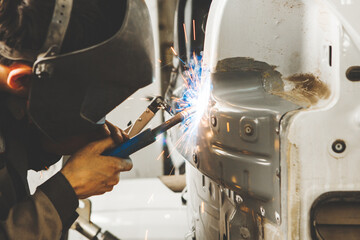 Young man in protective mask repairing an old car body in garage. Weld of vehicle.