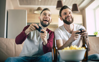 Wall Mural - Excited smiling men playing in video games on tv at home on the couch. Friends with joysticks play game with happy emotions on faces