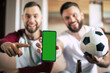 Close up mockup photo of green blank screen on the smart phone in hand of excited young bearded sports fans. Winning in bets
