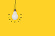 Bombilla de luz colgante sobre un fondo amarillo liso y aislado. Vista de frente y de cerca. Copy space