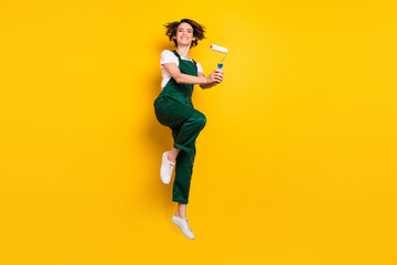 Canvas Print - Full size photo of young pretty smiling woman painter jumping with roller restoration isolated on yellow color background