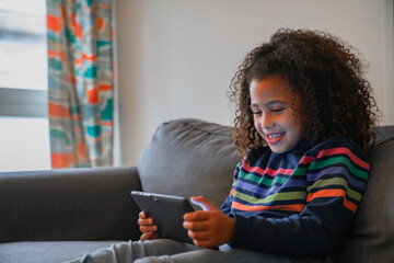 Side view of afro little girl on living room using tablet smiling having fun