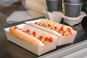 Two hot dogs in a cardboard box and two cardboard cups of coffee on the counter of a street food take-out cart. Traditional takeaway, street food, snacks.