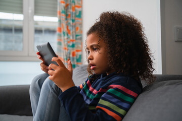 Side view of afro little girl on living room using tablet focused
