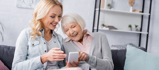 Woman pointing with hand at smartphone near elderly mother, banner