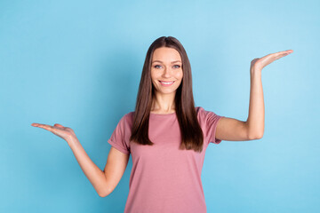 Photo of young happy charming woman hold hands empty space scales isolated pastel blue color background